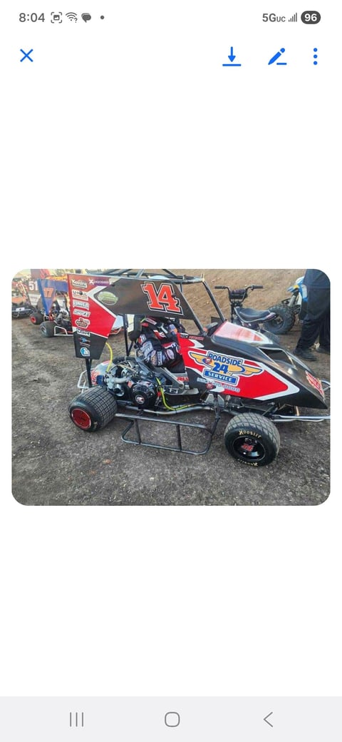 Red number 14 sprint racing car displayed at a pit area with crew members nearby