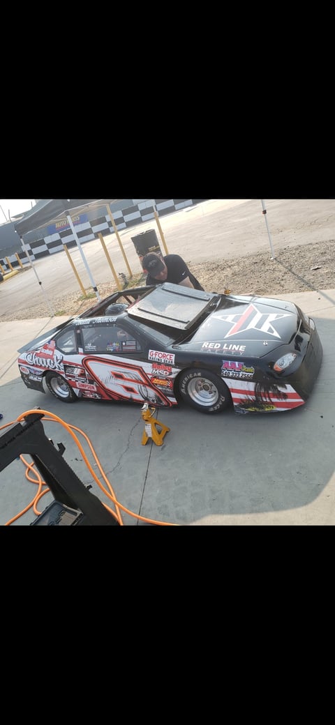 Black and white drag racing car with red graphics on concrete at a racetrack with checkered barriers