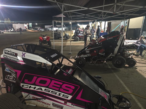 Pink and black go-kart with Joes Racing livery at night racing event under tent canopy with other karts and spectators visible in background